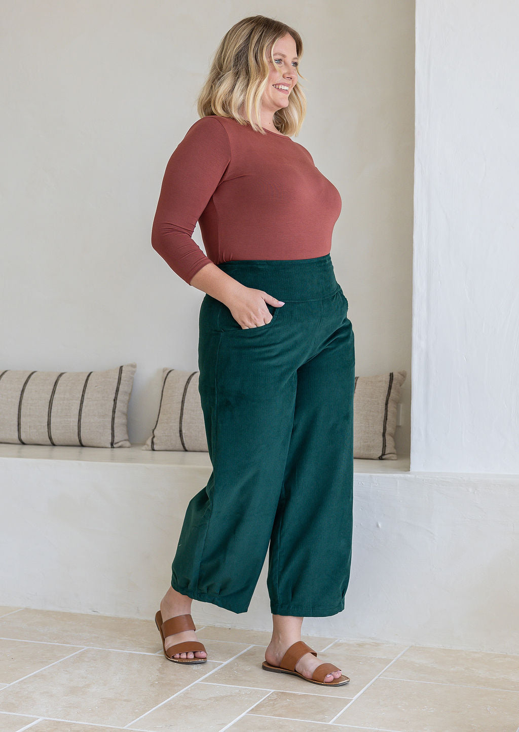 Model standing sideways wears corduroy wide leg pants with side zipper, pockets and small pleats at ankles.
