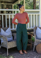 Woman posing in cotton corduroy wide-leg dark green pants with wide flat waistband, side zipper and small pleats at the ankles.