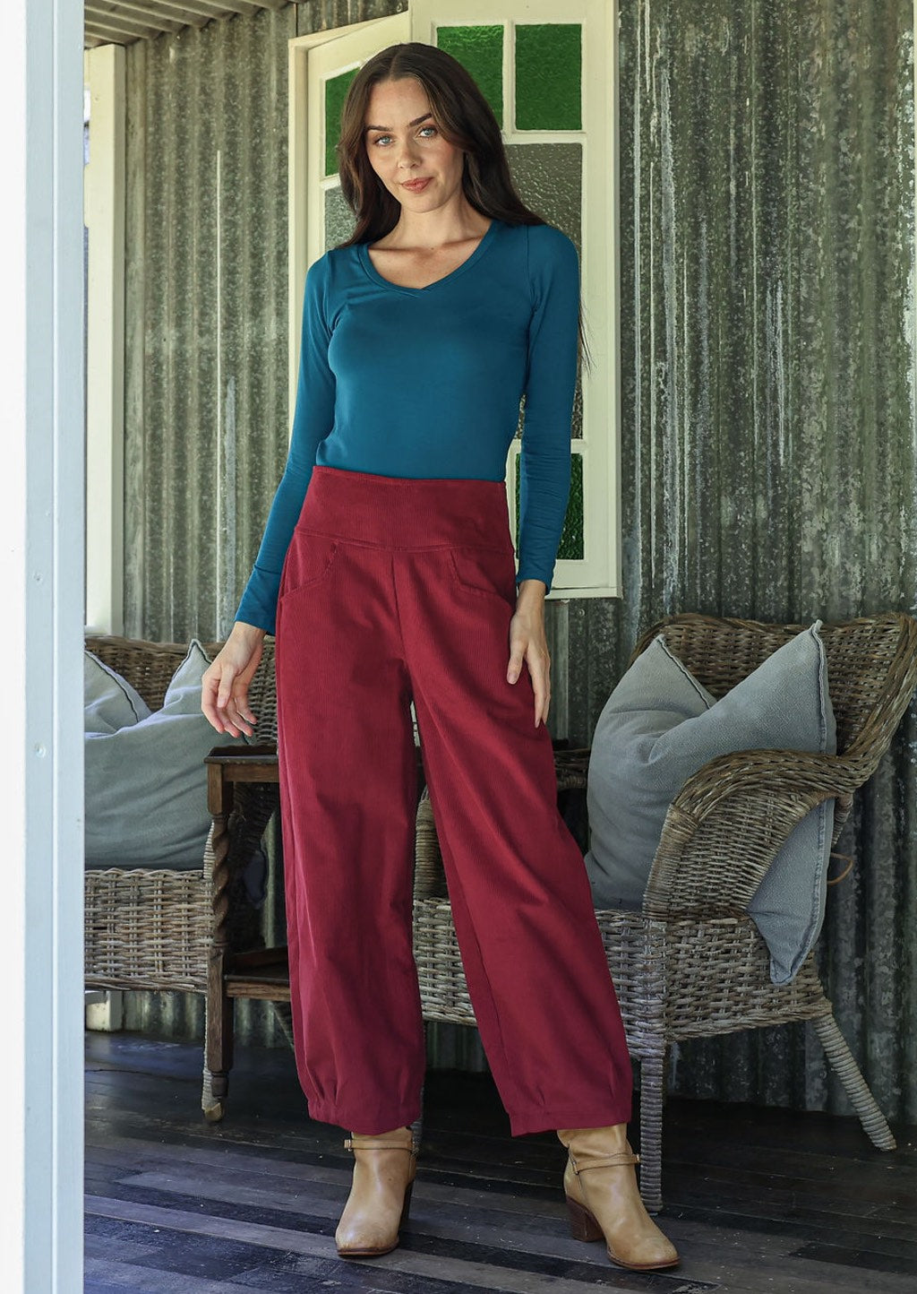 Woman wearing a blue top and red pants standing in a rustic indoor setting.