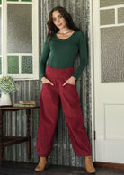 Woman posing in cotton corduroy wide-leg red pants with wide flat waistband, side zipper and small pleats at the ankles.