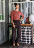 Woman posing in cotton corduroy wide-leg dark brown pants with wide flat waistband, side zipper and small pleats at the ankles.