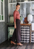 Woman wearing a cotton corduroy wide-leg dark brown pants, side zipper and small pleats at the ankles.