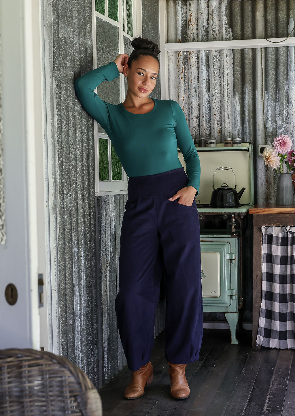 Woman posing in cotton corduroy wide-leg navy blue pants with wide flat waistband, side zipper and small pleats at the ankles.