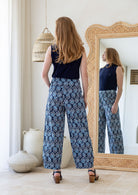 Model standing backwards wears 100% cotton wide leg pants with side zipper, pockets and small pleats at ankles.