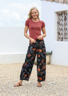 Woman wearing cotton wide leg pants in black based botanical print, paired with terracotta basic rayon top 