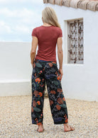 Model standing in a back pose wears wide leg cotton pants with pockets and side zipper in black based botanical queen protea print 