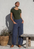 Woman posing in 100% cotton wide-leg navy based white strioed printed pants with wide flat waistband, side zipper and small pleats at the ankles.