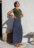 Model standing sideways wears 100% cotton wide leg pants with side zipper, pockets and small pleats at ankles.