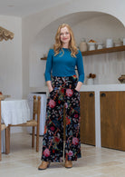 Woman wearing a basic top with black based multi-colour floral velvet wide leg pants with pockets and a side zip