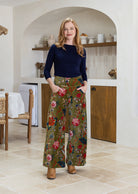 Woman wearing a green based multi-colour floral velvet wide leg pants with hands in pockets and a side zip
