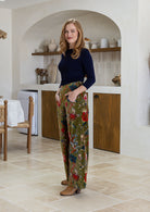 Woman standing sideways wearing a green based multi-colour floral velvet wide leg pants with basic navy top