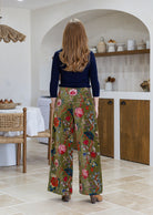 Woman standing backwards wearing a green based multi-colour floral velvet wide leg pants with wide waistband 