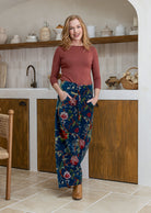 Woman in a terracotta basic top and floral velvet pants standing in a kitchen.
