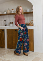 Woman standing sideways wearing a teal based multi-colour floral velvet wide leg pants with basic terracotta top