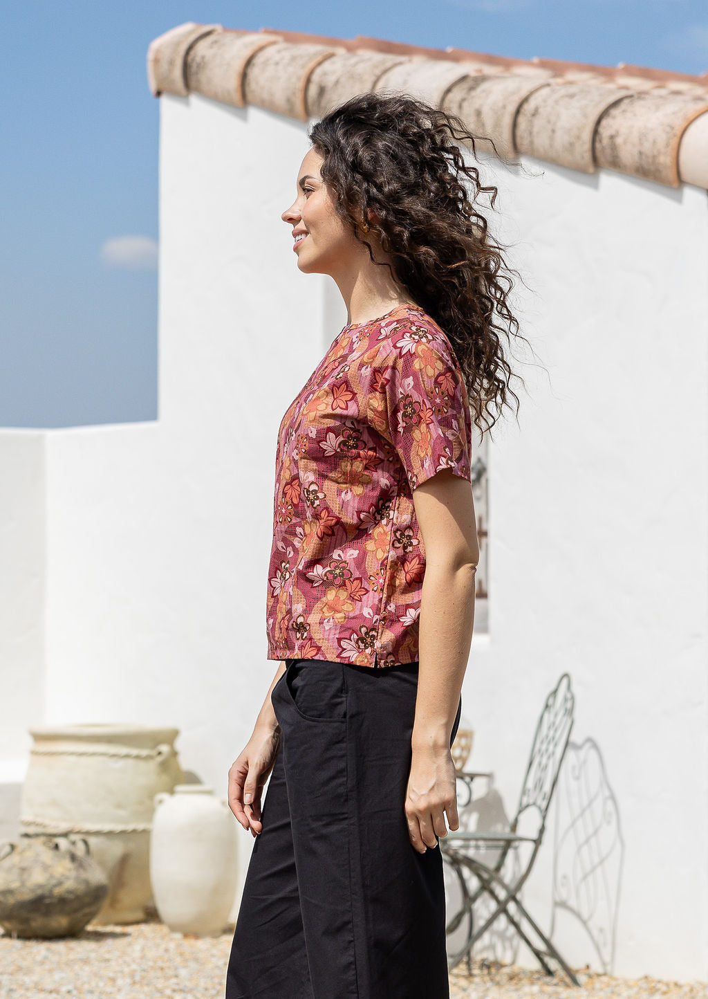 Woman stands sideways wearing black cotton pants with loose fitting Japanese style floral print cotton top with short sleeves and high round neckline 