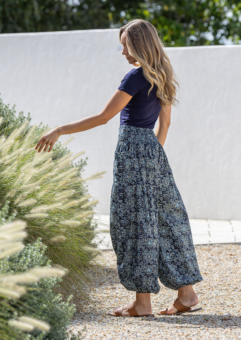Woman holding flowers wearing a 100% cotton floral blue harem pants with flat wide waistband in front and elastic at the back.