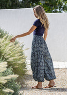 Woman holding flowers wearing a 100% cotton floral blue harem pants with flat wide waistband in front and elastic at the back.