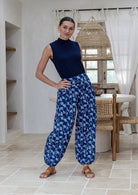 Woman wearing a basic top and blue based floral pants with wide elastic waist and ankles.