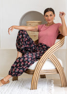 Woman wearing a cotton Black floral print harem pants with pink top seated in rattan chair