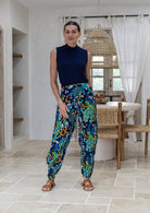 Woman modeling a sleeveless navy blue mock neck top and high-waisted, wide-leg cotton harem pants with a vibrant blue, green, and yellow peacock print