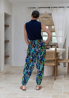 Back view of woman wearing cotton harem pants with a peacock print and elastic ruched back, paired with a sleeveless navy top. 