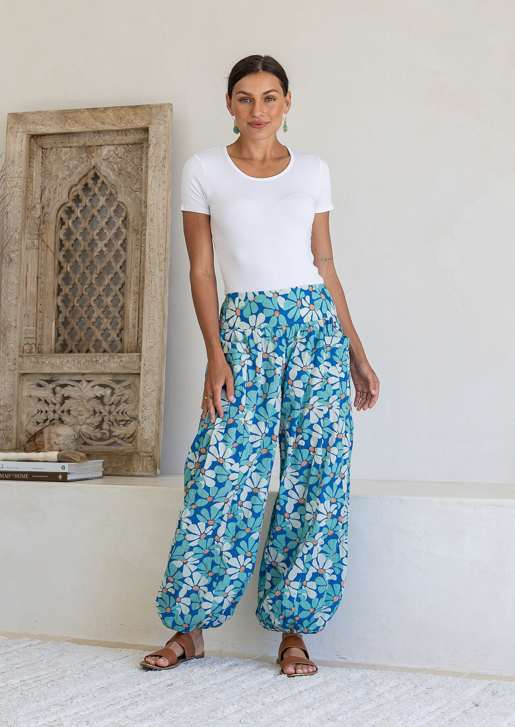 Woman wearing cotton harem pants in a blue daisy print, paired with a white t-shirt and tan sandals