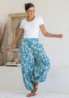 Woman poses in cotton harem pants in blue and aqua daisy print, paired with a white stretch rayon top