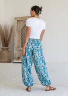 Back view of woman wearing cotton harem pants in blue daisy print with elastic shirring a back of waistband, paired with a white t-shirt
