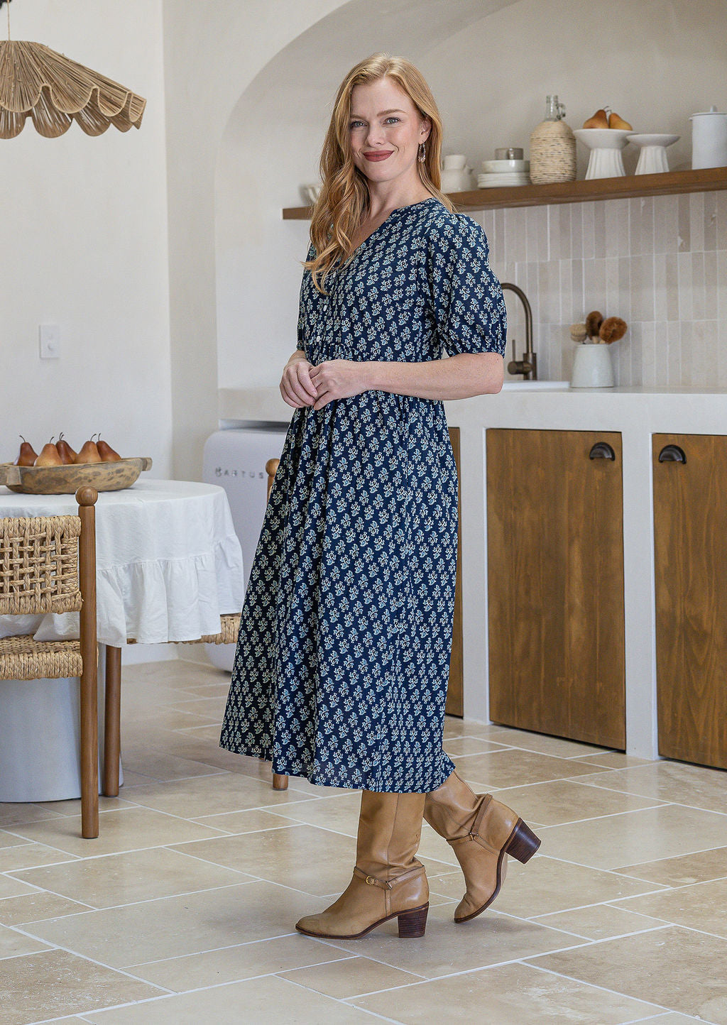 woman standing sideways wearing a 100% cotton dress in navy blue based floral print. 