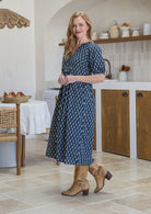 woman standing sideways wearing a 100% cotton dress in navy blue based floral print. 