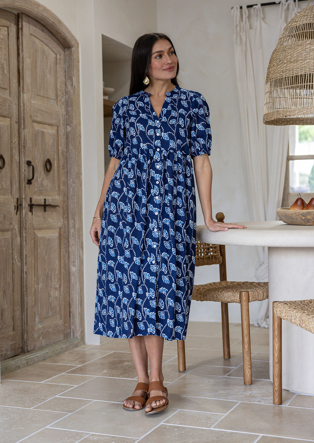 Woman in a navy based floral cotton button through dress with elbow length puffy sleeves and a V-neckline. 