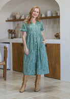 Woman wearing a sage green based floral cotton button through dress with one hand in hidden side pocket
