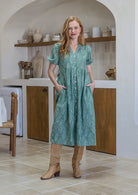 Woman in a sage green based floral cotton button through dress with elbow length puffy sleeves and a V-neckline.