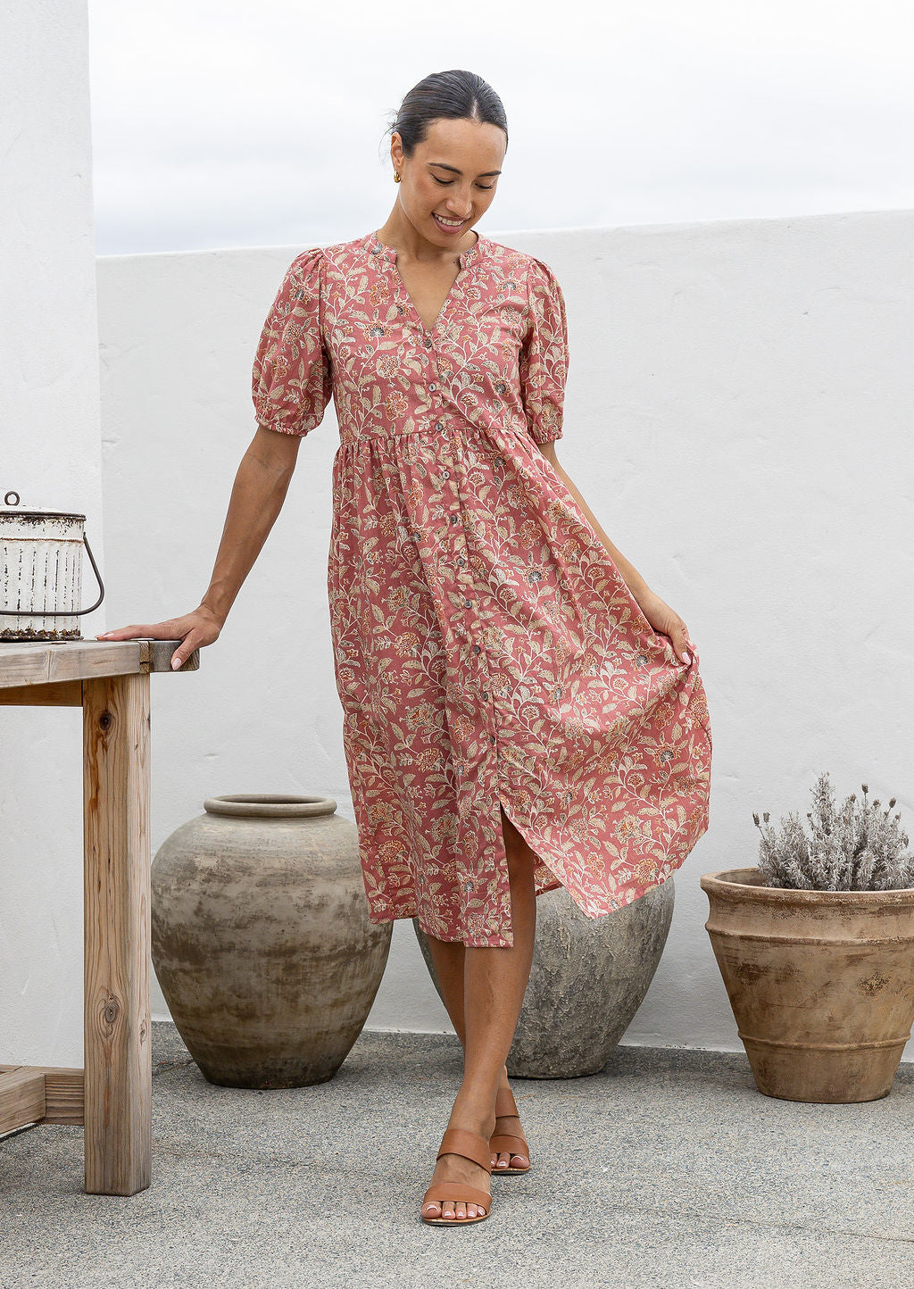 Woman in a pink floral cotton button through dress with elbow length puffy sleeves and a V-neckline. 