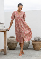 Woman in a pink floral cotton button through dress with elbow length puffy sleeves and a V-neckline. 