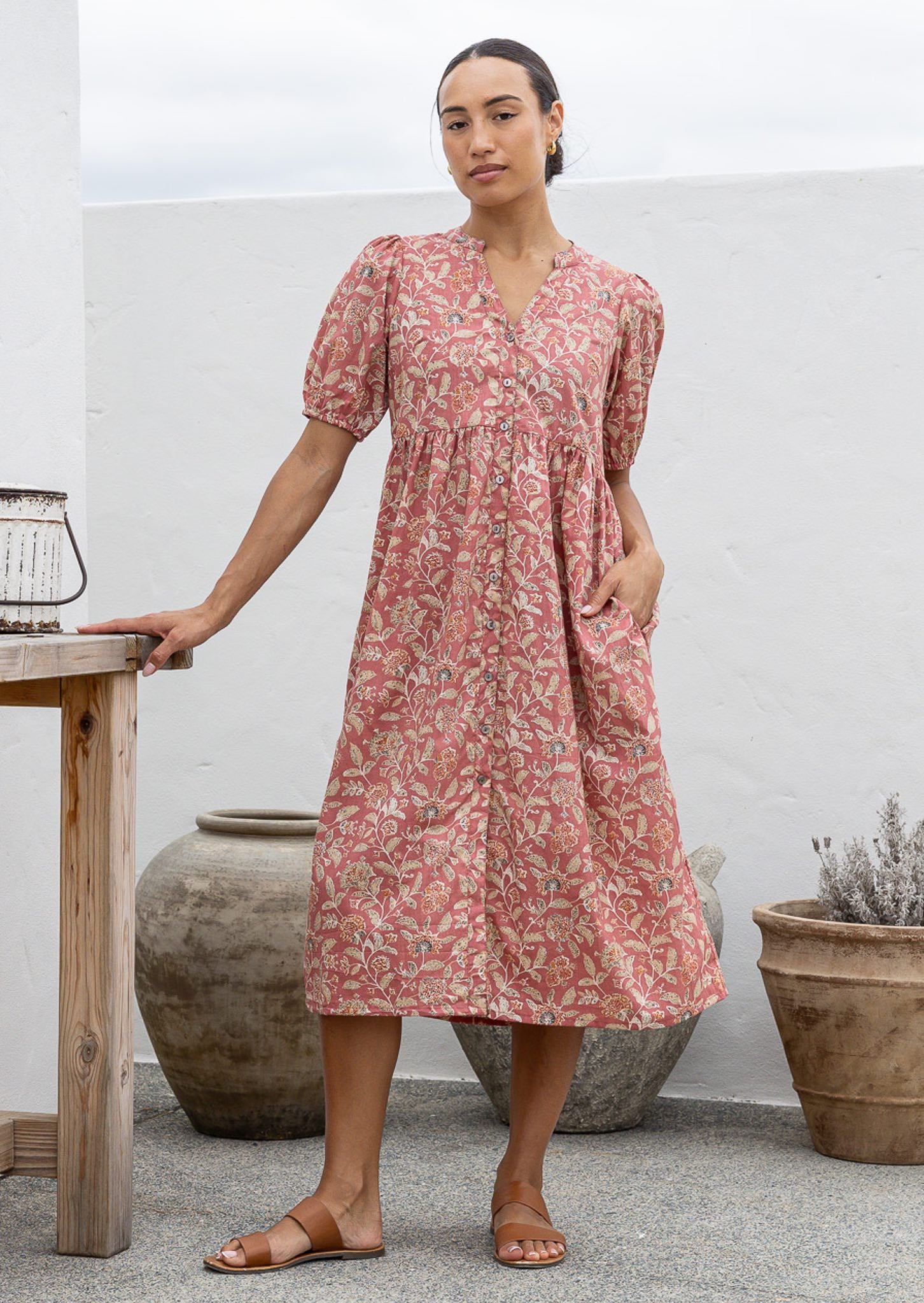 Woman wearing a pink floral cotton button through dress with one hand in hidden side pocket