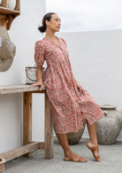 Woman in a dusky pink floral cotton midi length button through dress leaning against a wooden table