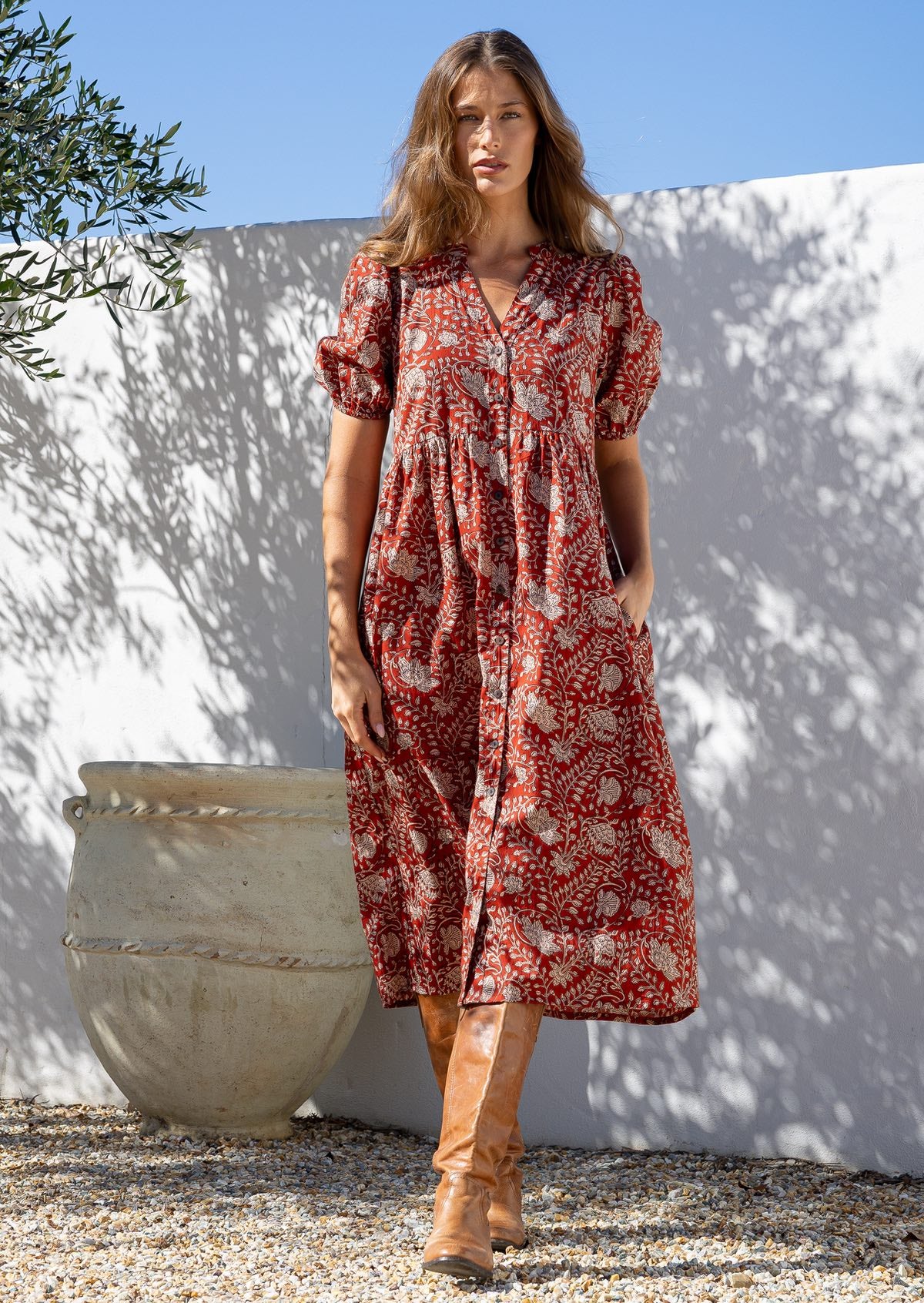 Woman wearing an earthy red floral cotton button through dress with one hand in hidden side pocket