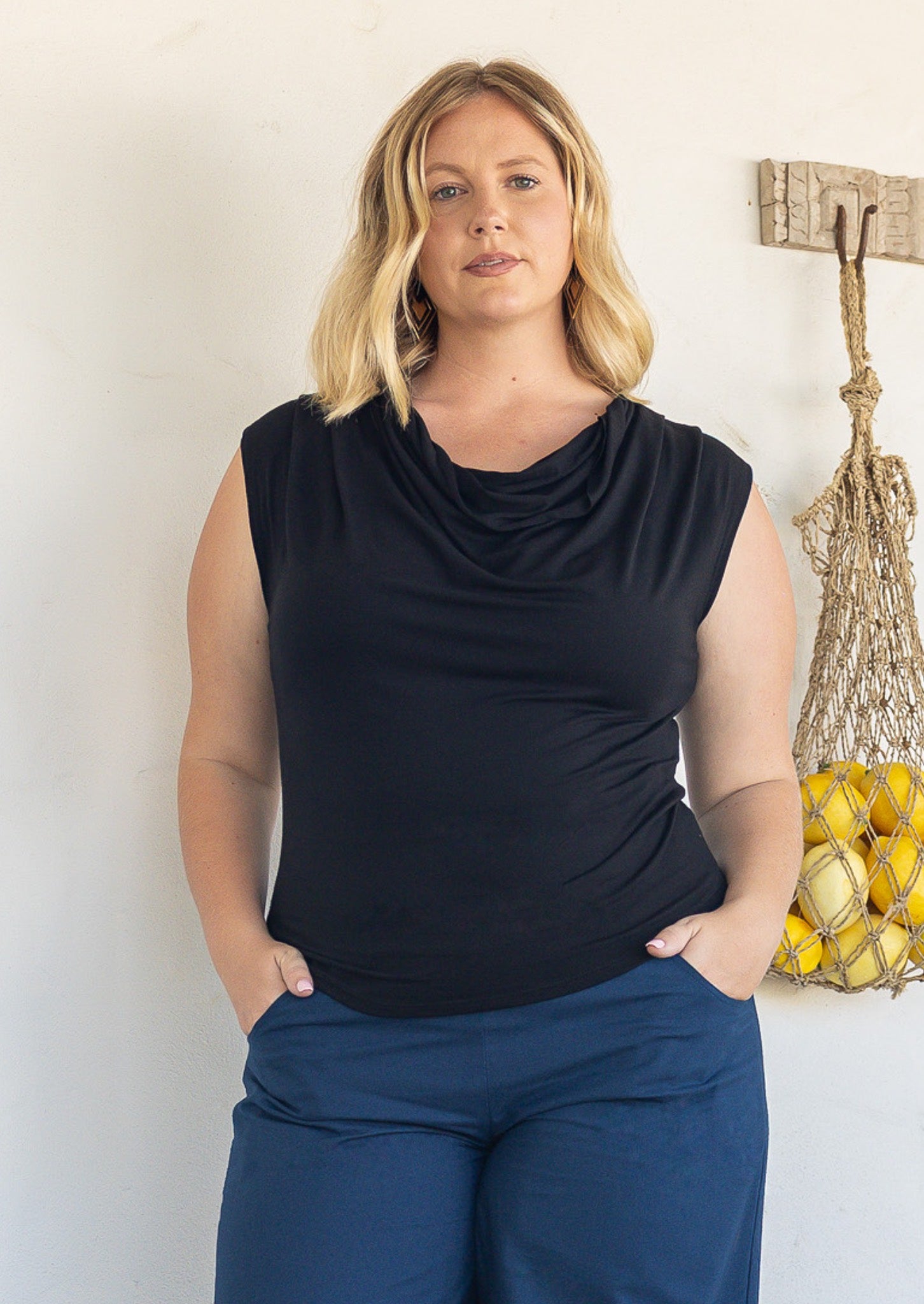 A woman wearing a black sleeveless stretch rayon cowl-neck top and navy blue pants