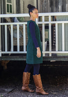 Woman wearing a green dress and brown boots standing in front of a white fence.