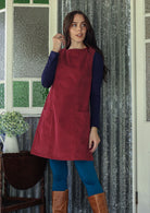 Woman wearing a red corduroy tunic over a blue leggings and a top in a room with patterned curtains.