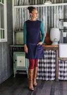 Woman wearing a navy tunic over a leggings and a top in a rustic setting.