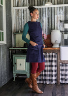 Woman in a blue dress and red leggings standing in a rustic kitchen.