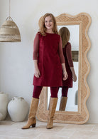 Woman poses in cotton corduroy tunic in cabernet paired with tan boots and leggings