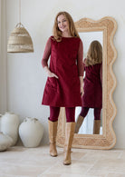 Woman poses in cotton corduroy tunic in cabernet with one hand in pockets styled with leggings and tan boots