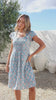 Video of a woman wearing a in a 100% cotton blue based floral dress with round neckline and cap sleeves