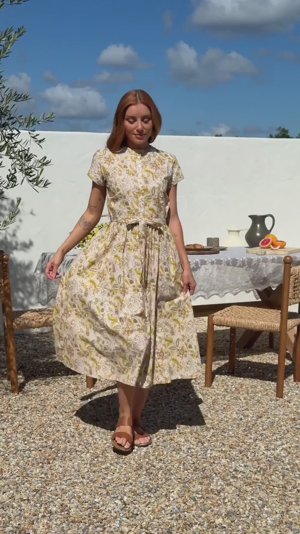 Video of a woman wears retro style cotton button through midi length dress with high round neckline, short sleeves and a removable waist tie.