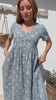 Video of a woman standing in a 100% cotton floral print dress with a V-neckline, short sleeves, pockets, and buttons through to the knee.