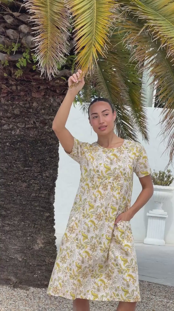 Video of a woman wearing a cream based cotton floral short sleeve dress with round neckline