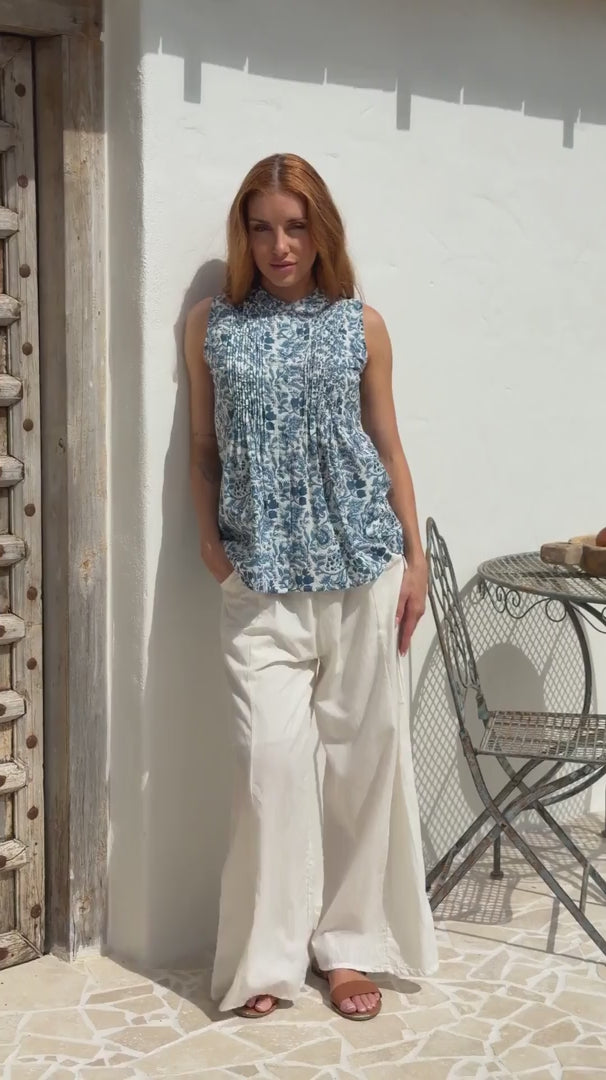 Video of a woman wearing a 100% cotton white based blue floral sleeveless top with small pleated design, and buttoned mandarin collar.